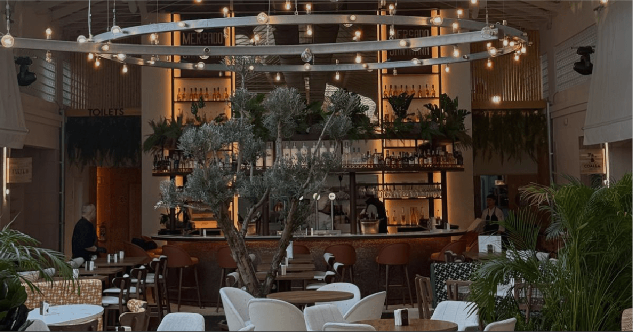 Interior de Mercado Santa Ana, con su gran olivo y la barra central iluminada