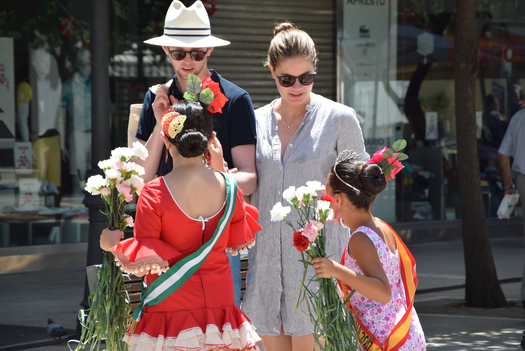 Niñas con traje de flamenca entregan claveles a visitantes durante el Día del Turista en Estepona