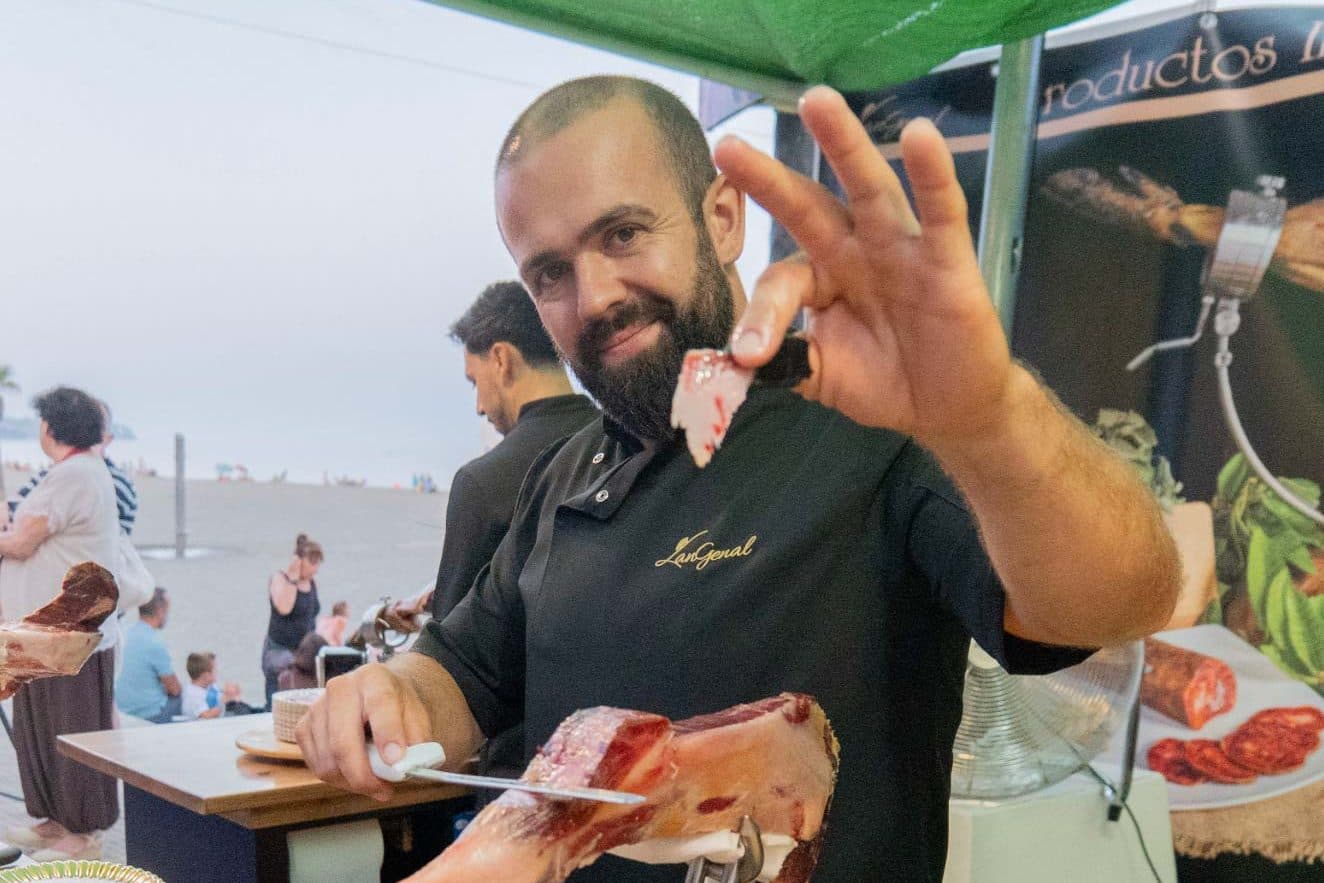 Cortador de jamón trabajando una pieza en directo en un evento gastronómico al aire libre en Estepona