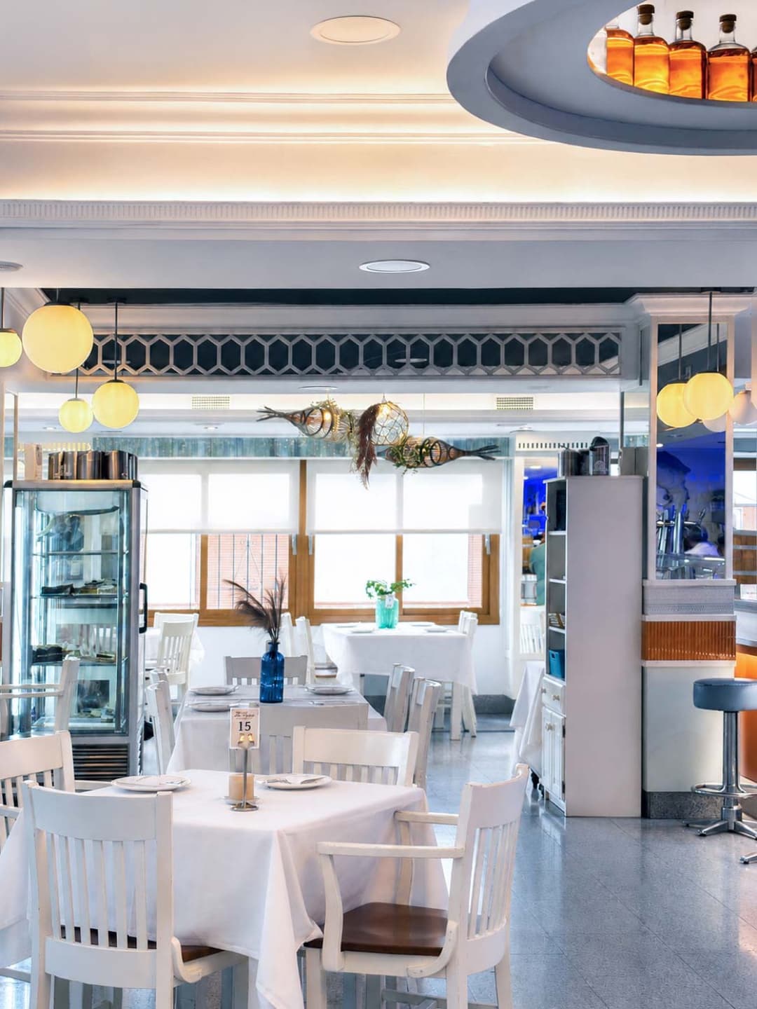 Comedor blanco de La Palma con mesas vestidas de lino, vitrina refrigerada y peces decorativos