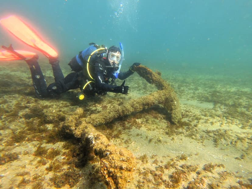 Buceador de Estepona Dive Center señalando un ancla antigua cubierta de fauna marina