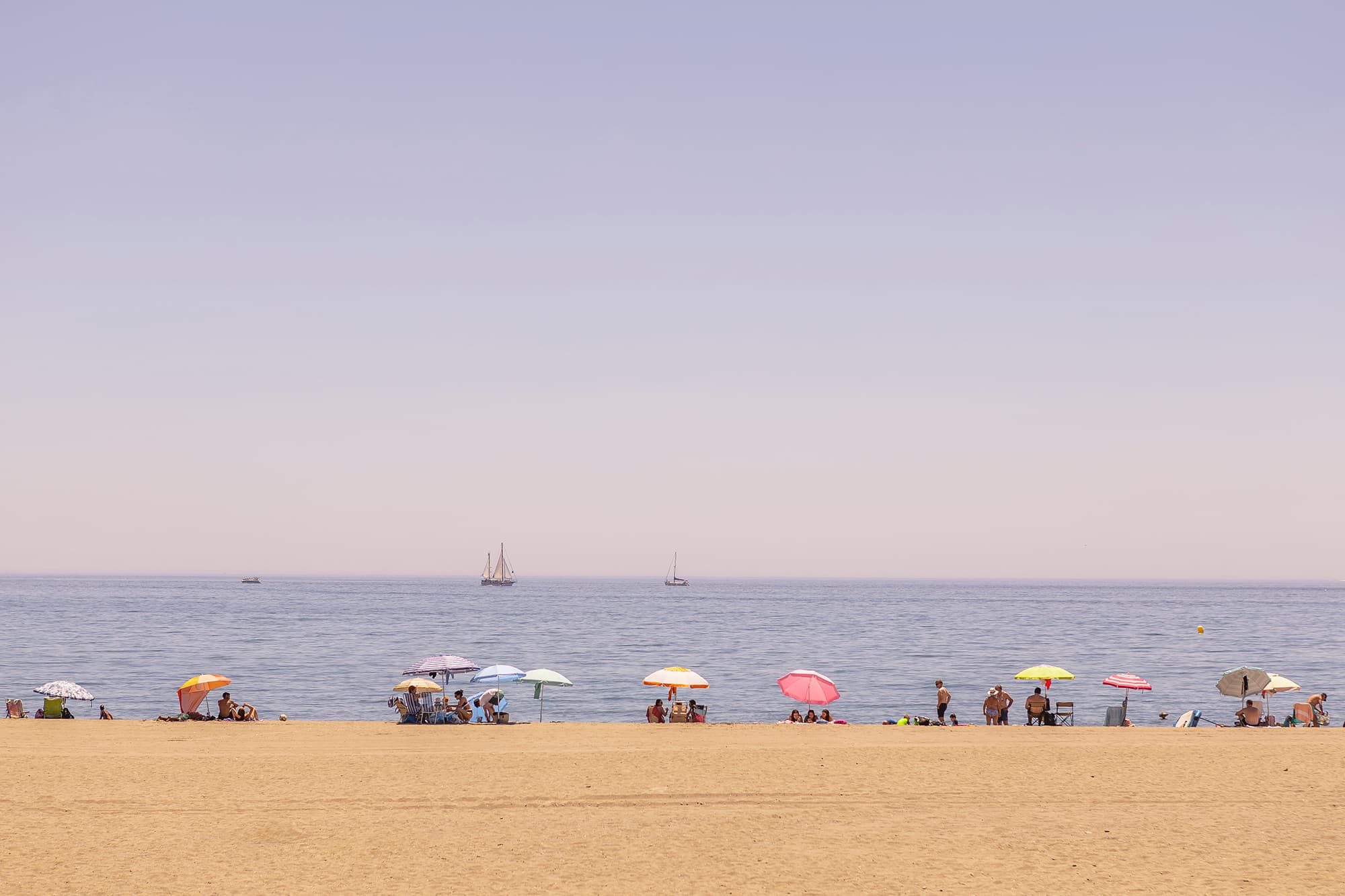 Beach in Estepona with parasols and sailboats in the background.