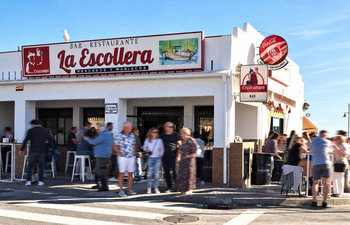 Fachada de Bar Restaurante La Escollera, pescados y mariscos, con terraza llena junto al Puerto Pesquero de Estepona